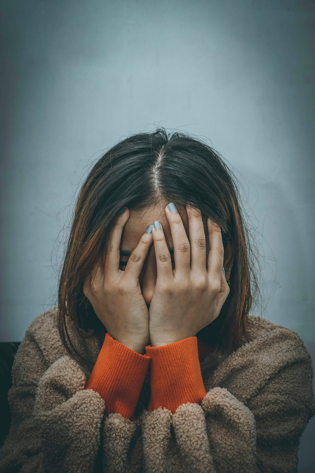woman in brown sweater covering her face with her hand